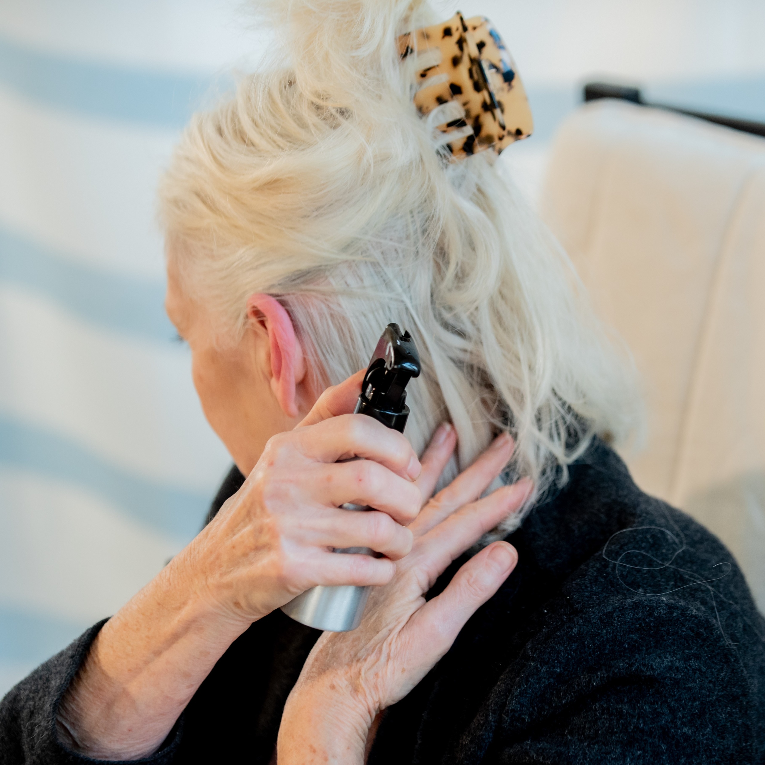 A woman uses a small spray bottle with water to wet her hair before using the scalp cooling machine