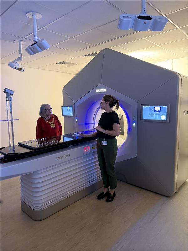 The Lord Mayor of Liverpool is being shown a large radiotherapy treatment machine. She is wearing gold chains of office. 