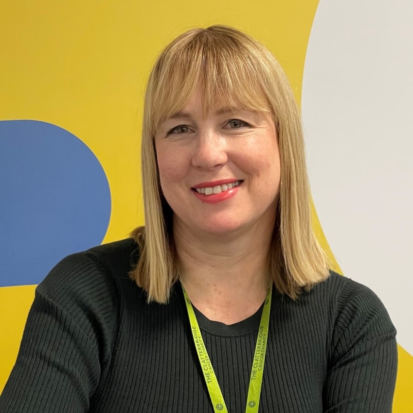 Picture of Liz Bishop. She is smiling and is sitting in front of a bright yellow wall. Liz has shoulder length blonde hair with a fringe. 