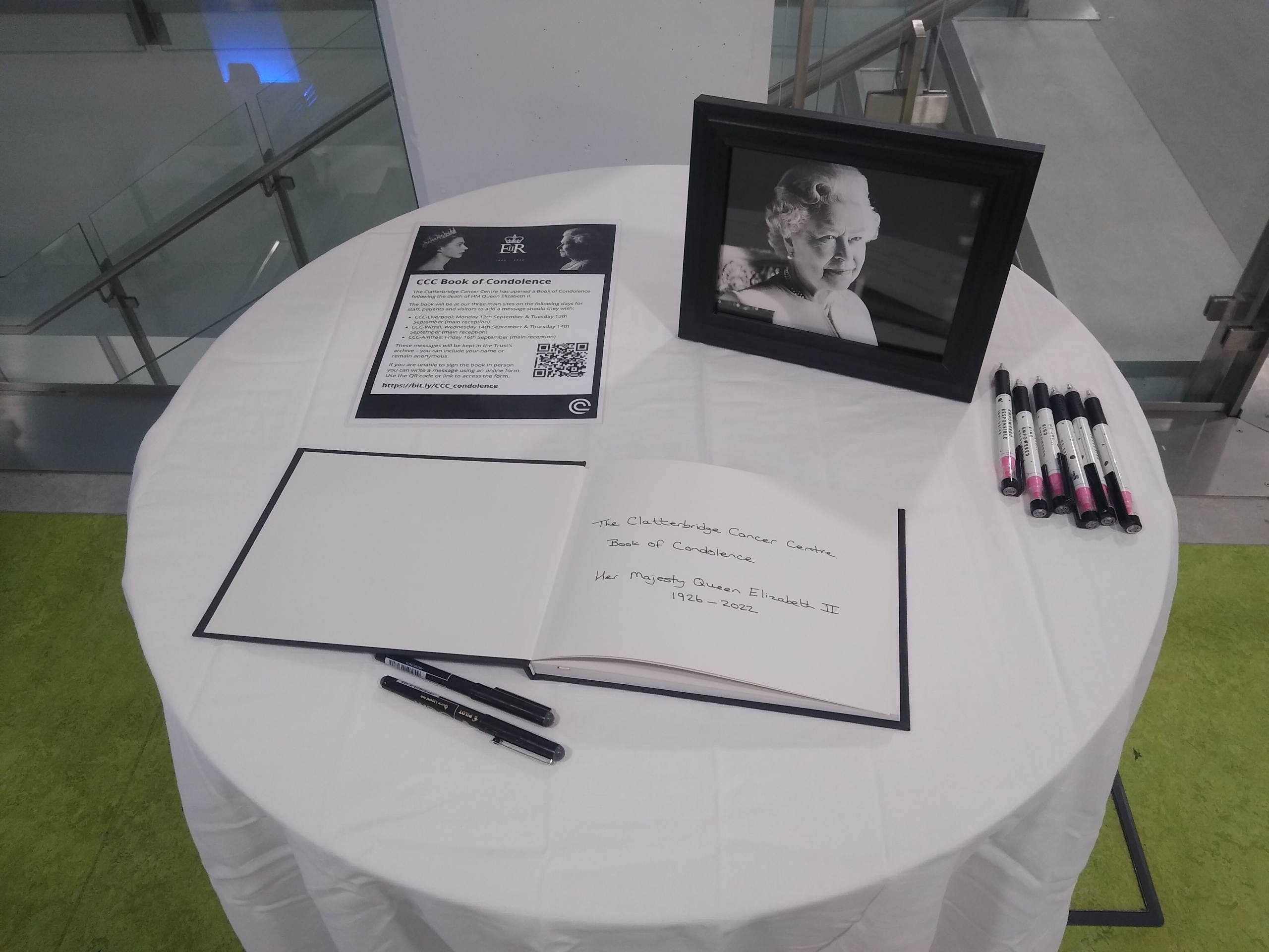 Table in CCC-Liverpool hospital main reception with a portrait of HM The Queen, the book of condolence, pens and information about how people can also sign the book online.