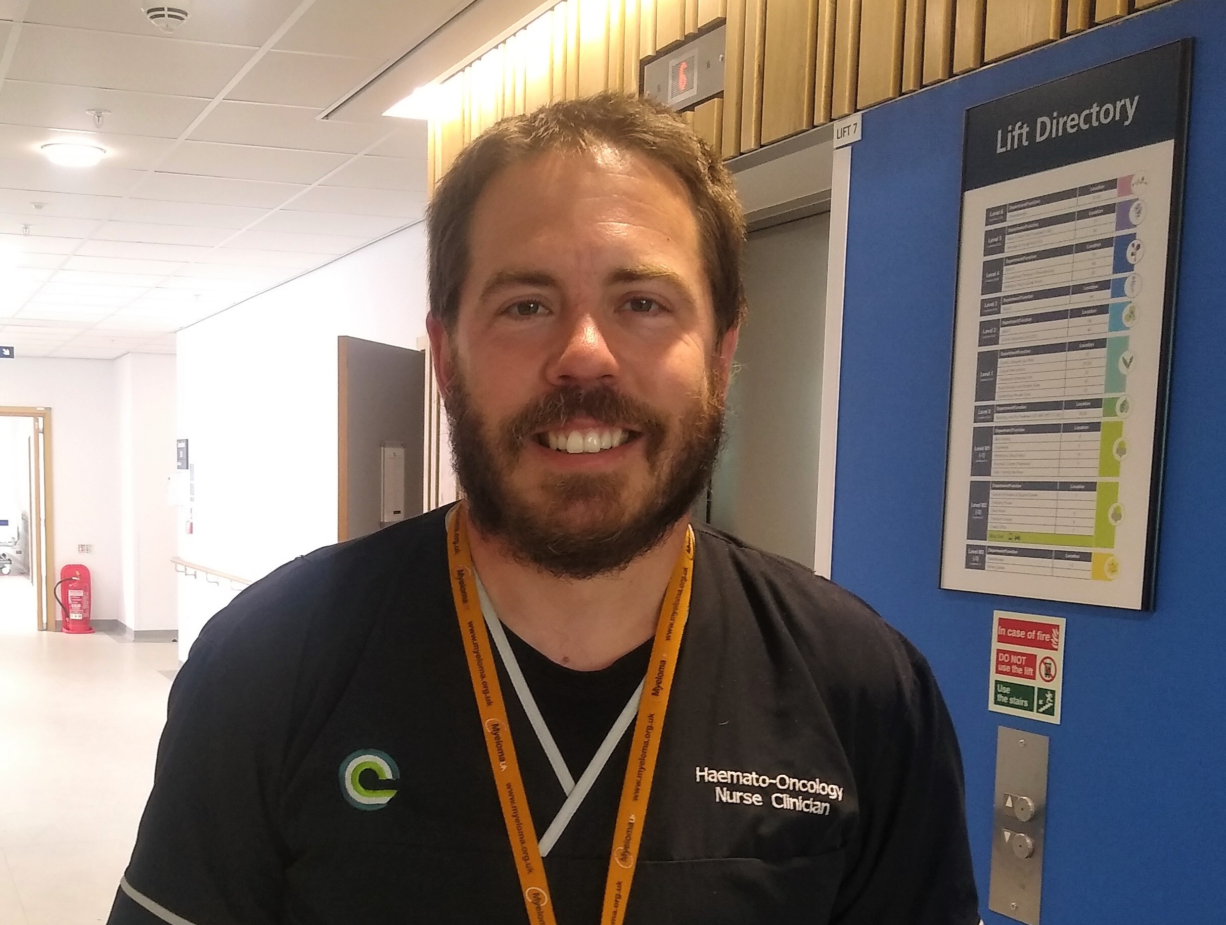 Picture of a male nurse, Craig Simon, in our hospital in Liverpool. He is wearing dark blue scrubs and smiling. 