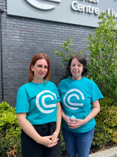 Two female volunteers in bright teal T-shirts standing outside the Liverpool cancer centre