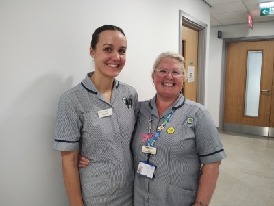 Nurses Chelcie and Jo both have blue and white striped uniforms and are standing in a hospital corridor