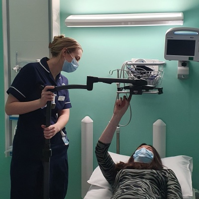 Patient lying flat on hospital bed but able to use a tablet (e.g. iPad-style device) on a stand that means the tablet is over her at eye level