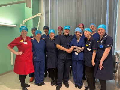 Members of our Interventional Radiology and Clinical Interventions Team stand in a hospital room. They are wearing scrubs and different coloured cotton scrub caps with their names on them