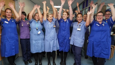 The Delamere chemtherapy team celebrating - they are in hospital uniforms and are waving their arms in the air and smiling