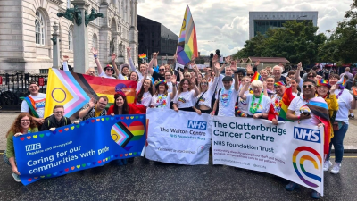 A photo of local NHS Trust staff attending Liverpool Pride 2024. Staff are holding Trust banners and wearing colourful clothing