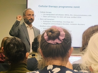 Dr Muhammad Saif presents at the CAR-T open evening. A large screen behind him has information about cellular therapies, linked to his talk