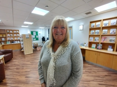 Rosslyn is standing in the hospital's cancer information centre. There are information booklets and leaflets on shelves around the room and tables and chairs where people can sit and chat